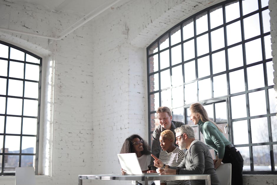 Group of diverse colleagues of different ages discussing business ideas while working on laptop in creative workplace and looking at screen during work